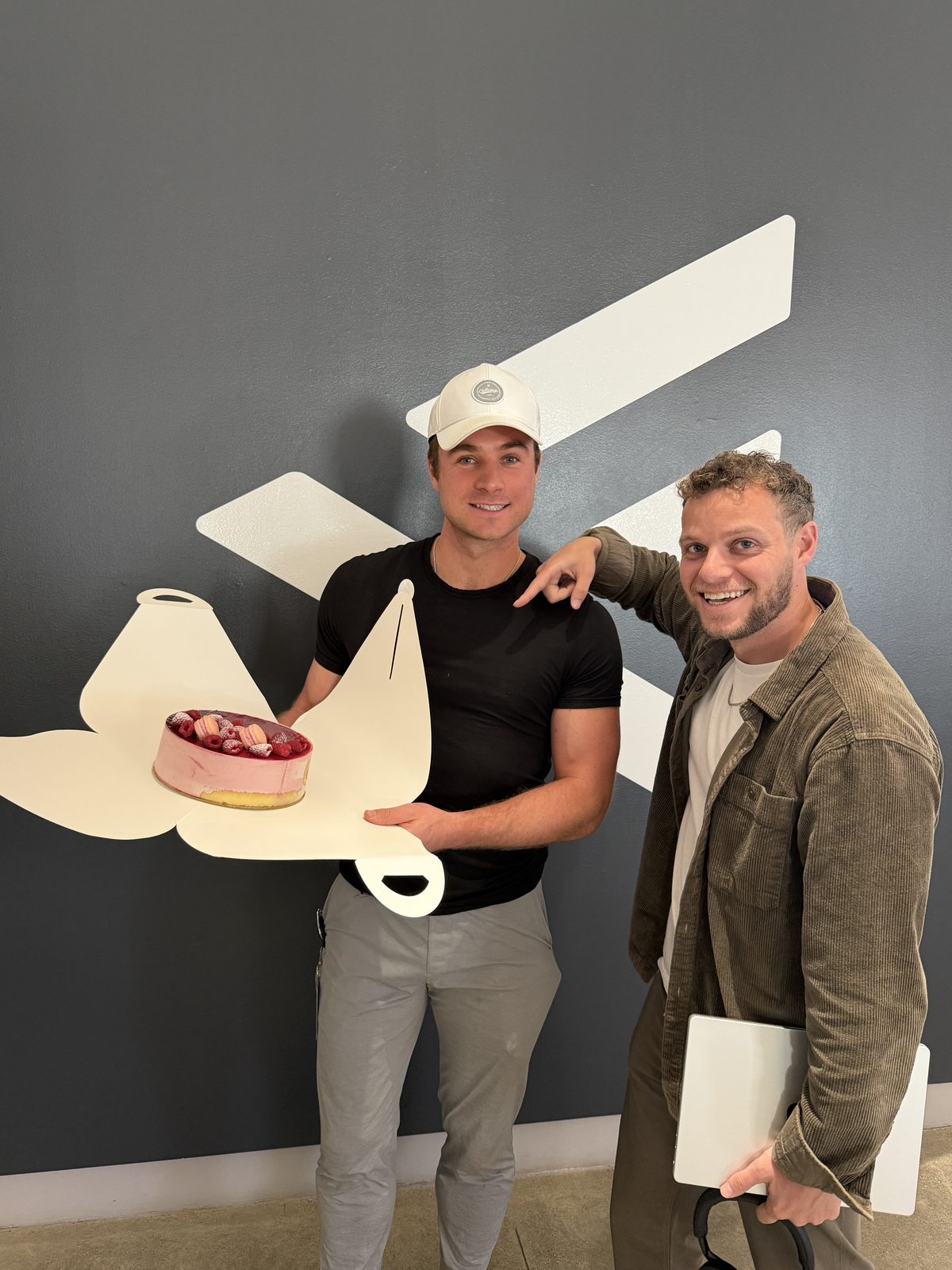 Alex Carrabre at F.inc holding a pink cheesecake coldcake on an F-shaped board, F.inc graphic wall behind him